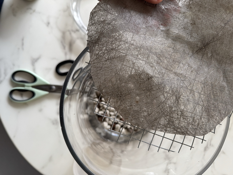 hardware mesh and garden cloth sitting above glass container with scissors on marble table
